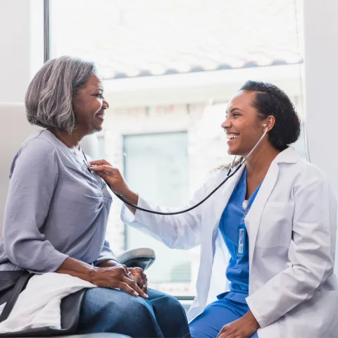 Doctor listening to an older woman patient's heart.
